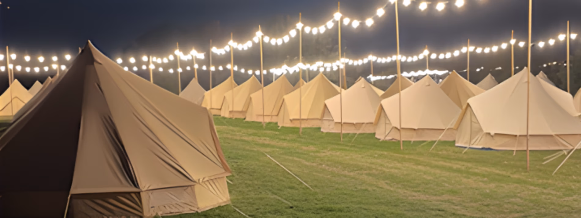 Bell Tents in rows on the fine mown grass of the Fields of LodeStar Festival late at night with high bamboo canes supporting festoon lights creating a magical atmosphere adding to the spiritual feeling people get when here.